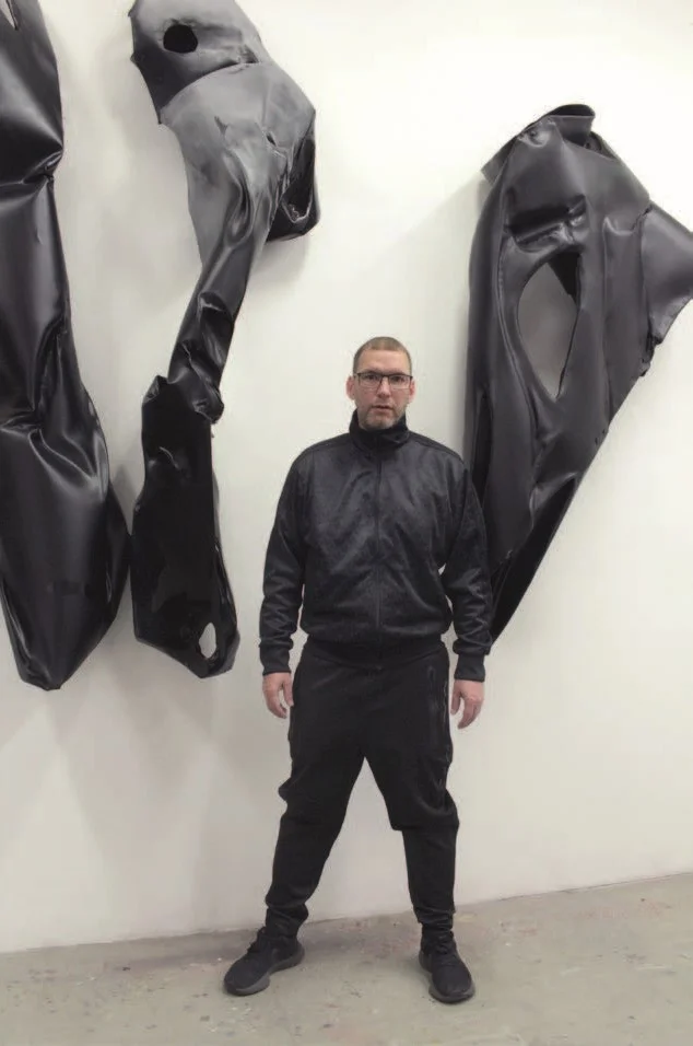 The artist stands in front of an artwork in a gallery