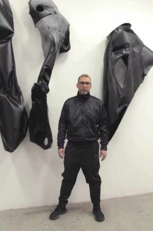 The artist stands in front of an artwork in a gallery